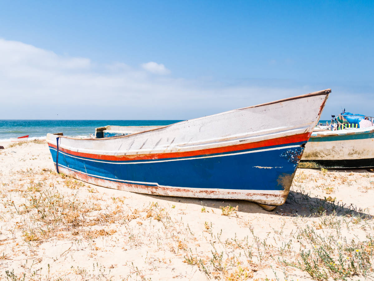 Barcas en la arena de una playa de Huelva, con el mar y el cielo azul de fondo