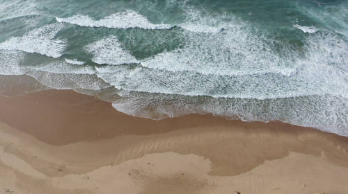 Vista cenital de la Praia do Amado, en Aljezur. Aparece la arena en la parte inferior de la imagen y las olas que rompen en la orilla en la mitad superior.